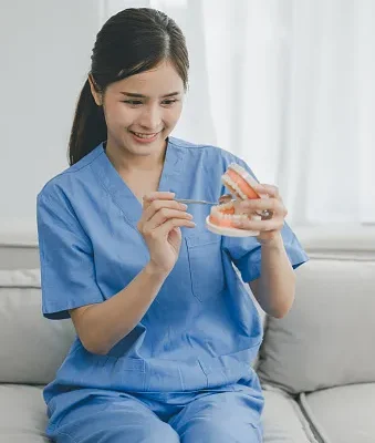 a dentist holds denture model mouth mirror for teaches elderly woman how to take care of her