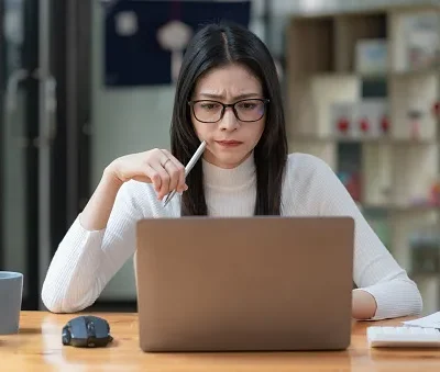 concerned female worker looking at laptop screen suspiciously thinking about problem solving